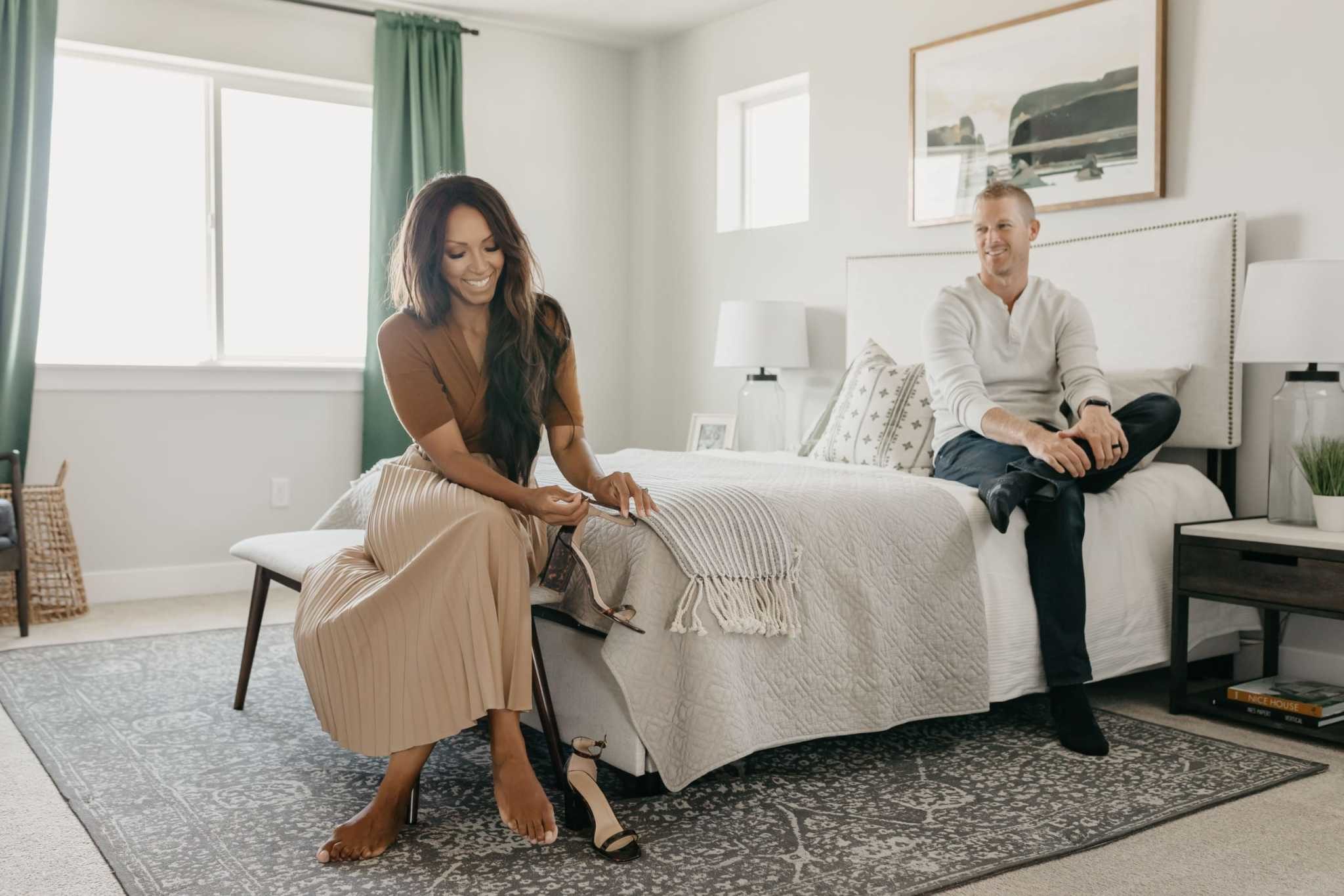 young biracial couple sitting on a bed and smiling