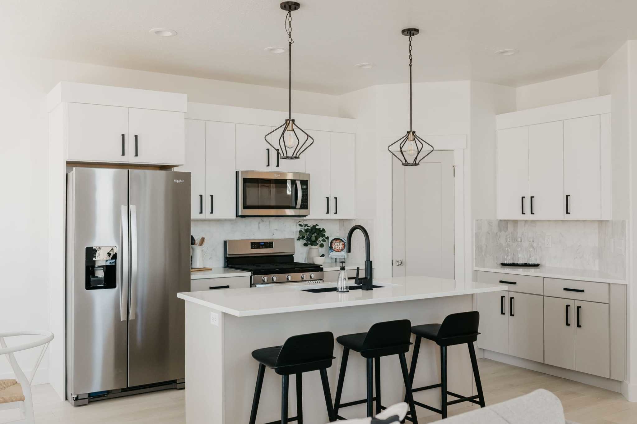 black pendant lights over a white kitchen island with black stools
