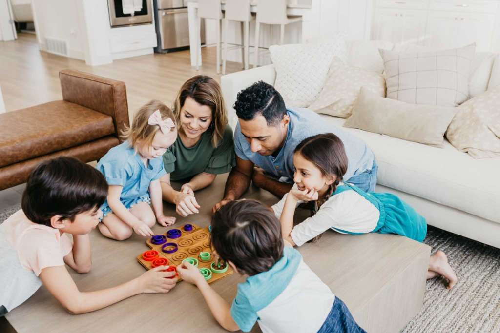 two young parents playing a board game with four young children
