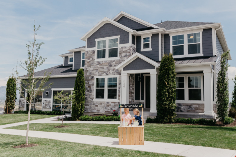 Beautiful two-story home with two little girls running a lemonade stand out front